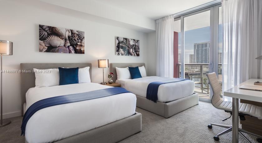 A bedroom features two beds, a desk, and a balcony with a city view — 2602 E Hallandale Beach Blvd # R310, Hallandale Beach FL 33009, HALLANDALE BEACH, FL