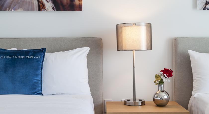 A bedroom features two beds with gray headboards, a bedside lamp, and a small vase — 2602 E Hallandale Beach Blvd # R310, Hallandale Beach FL 33009, HALLANDALE BEACH, FL