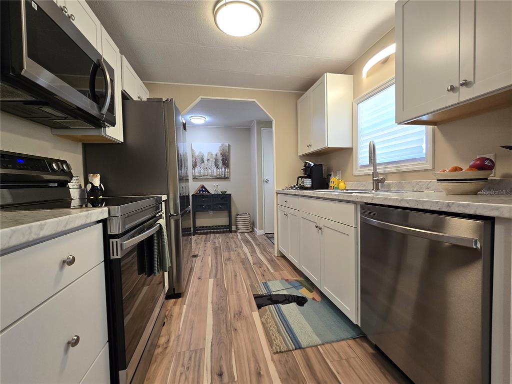 A kitchen features white cabinets, stainless steel appliances, and wood-look flooring — 6710 36TH AVENUE E UNIT 145, PALMETTO, FL
