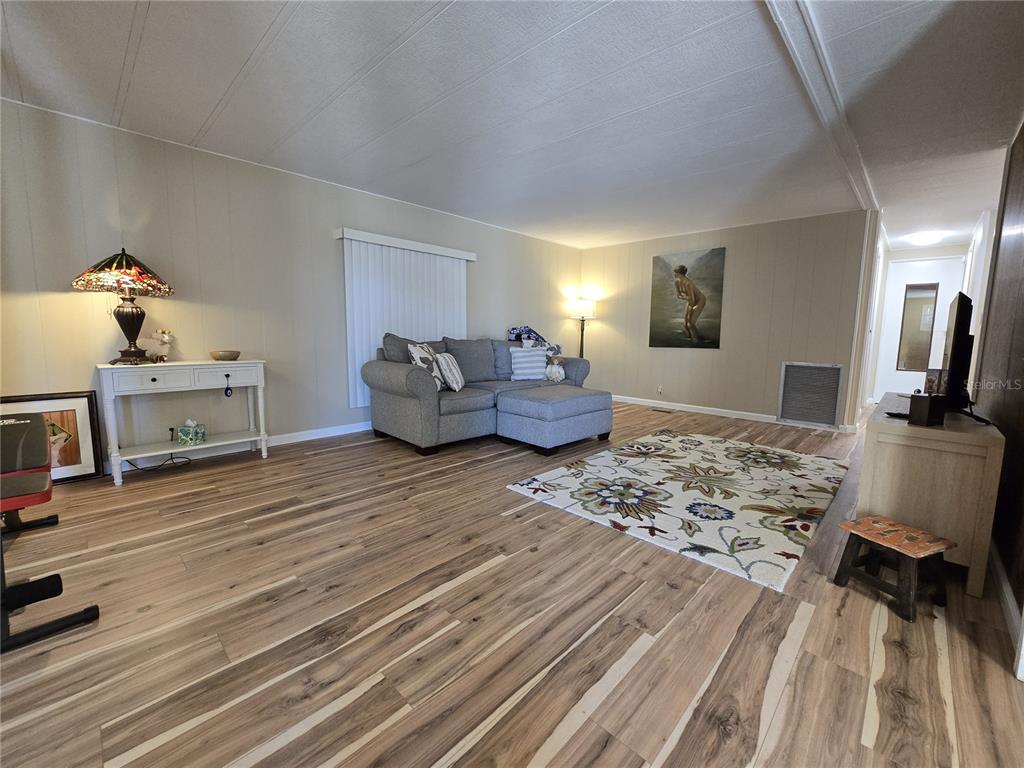 A living room features wood-look flooring, a gray sectional sofa, and a patterned area rug — 6710 36TH AVENUE E UNIT 145, PALMETTO, FL