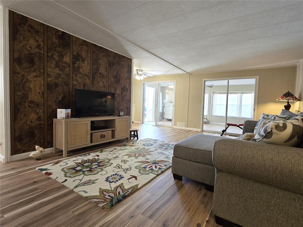 A living room features wood-paneled walls, a floral area rug, and a light-colored media console — 6710 36TH AVENUE E UNIT 145, PALMETTO, FL