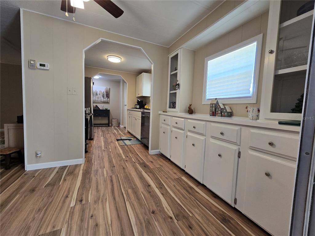 A dining area with wood-look flooring leads into a kitchen with white cabinetry — 6710 36TH AVENUE E UNIT 145, PALMETTO, FL