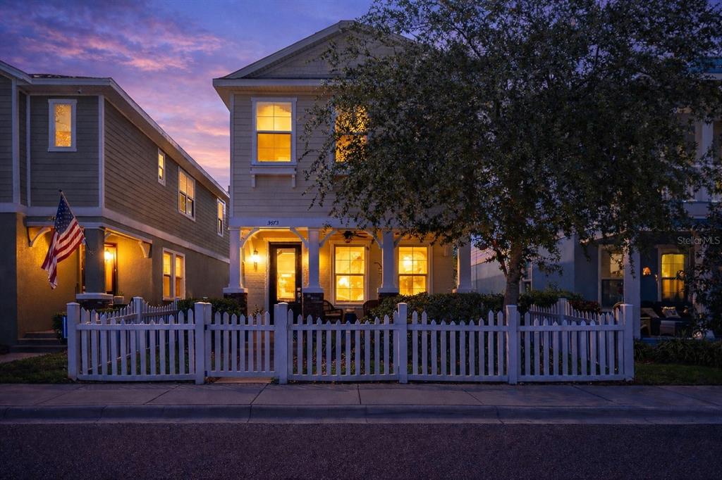 A two-story house with a white picket fence and a front porch at dusk — 3473 BUMELIA LANE, NEW PORT RICHEY, FL