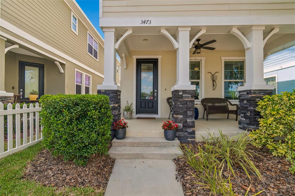 A front porch with stone pillars, a dark door, and a white picket fence — 3473 BUMELIA LANE, NEW PORT RICHEY, FL