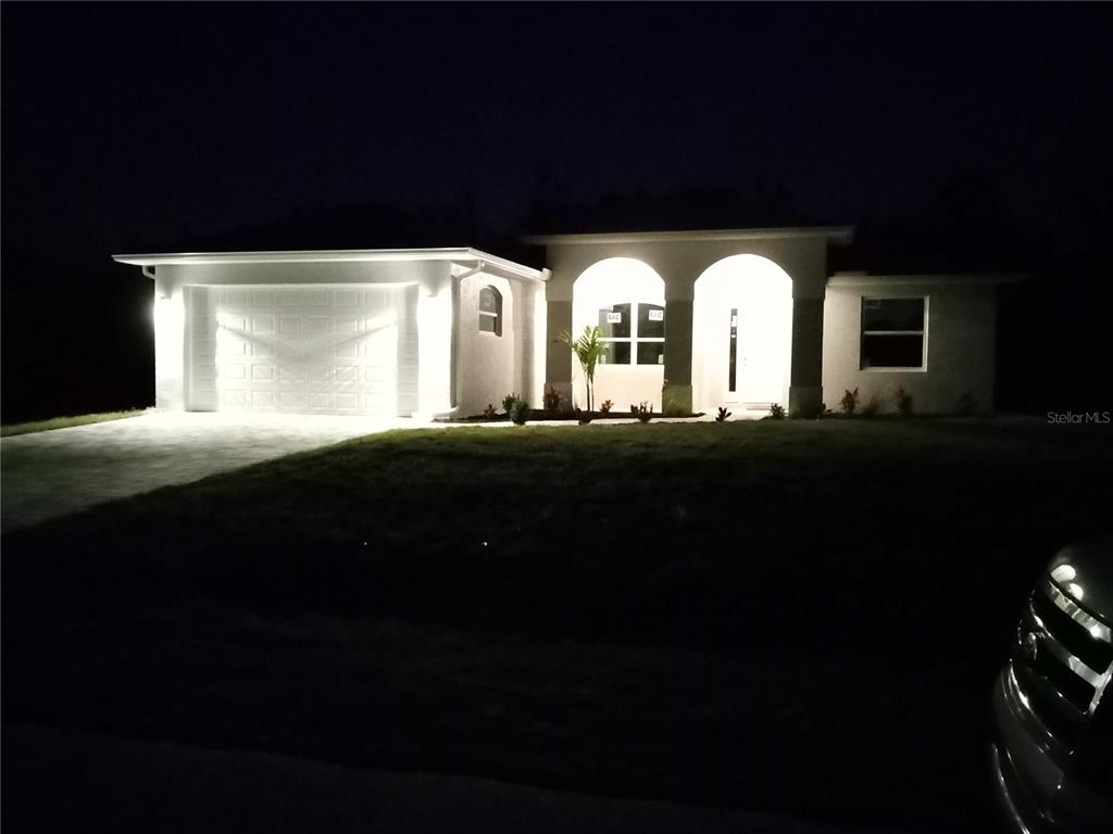 A single-story house with a garage and arched entryway is illuminated at night — 7197 TREADWAY ROAD, PORT CHARLOTTE, FL