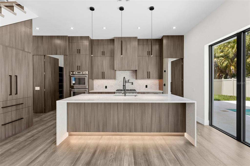 A modern kitchen features wood-grain cabinets, a large white island, and a sliding glass door — 2604 SYDELLE STREET, SARASOTA, FL