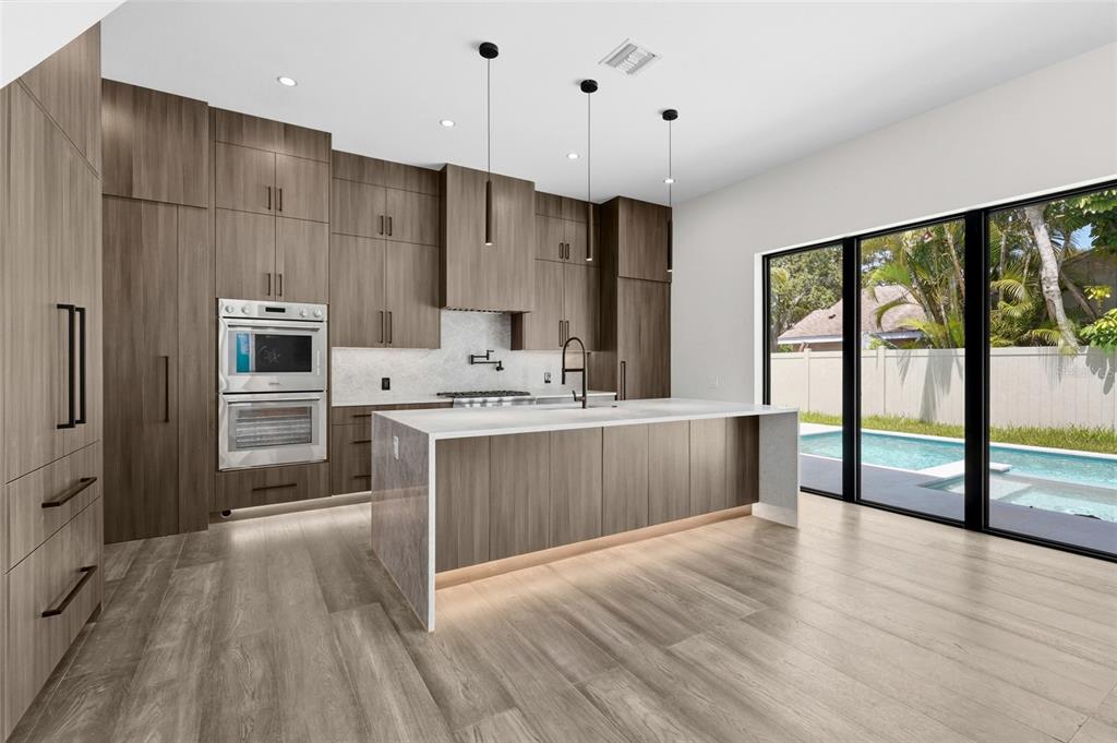 A modern kitchen features wood-grain cabinetry, a large waterfall island, and sliding glass doors to a pool — 2604 SYDELLE STREET, SARASOTA, FL