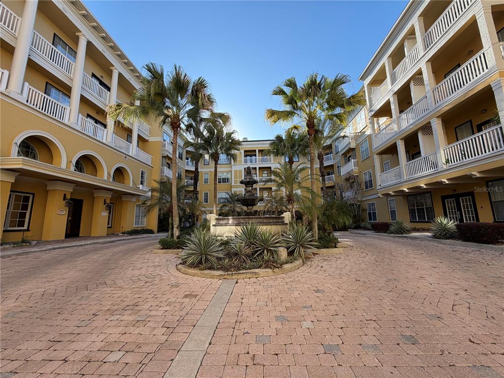 A paved courtyard features a central fountain surrounded by palm trees and yellow apartment buildings — 860 N ORANGE AVENUE UNIT 301, ORLANDO, FL