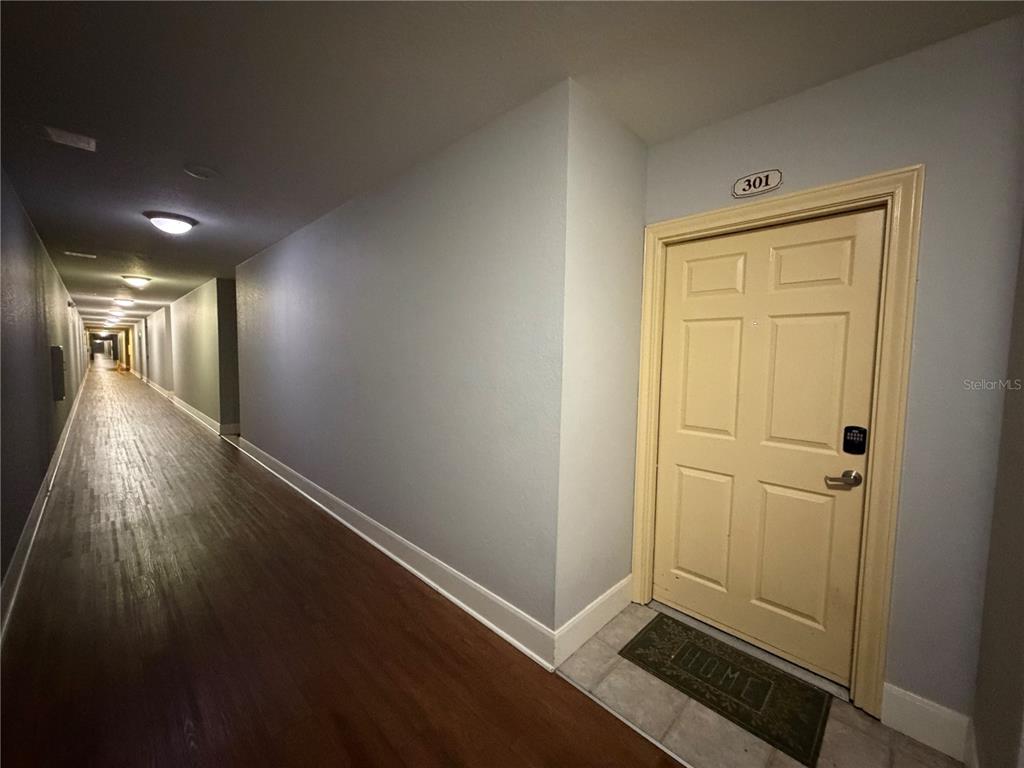 A long hallway with wood-look flooring leads to a beige apartment door numbered 301 — 860 N ORANGE AVENUE UNIT 301, ORLANDO, FL