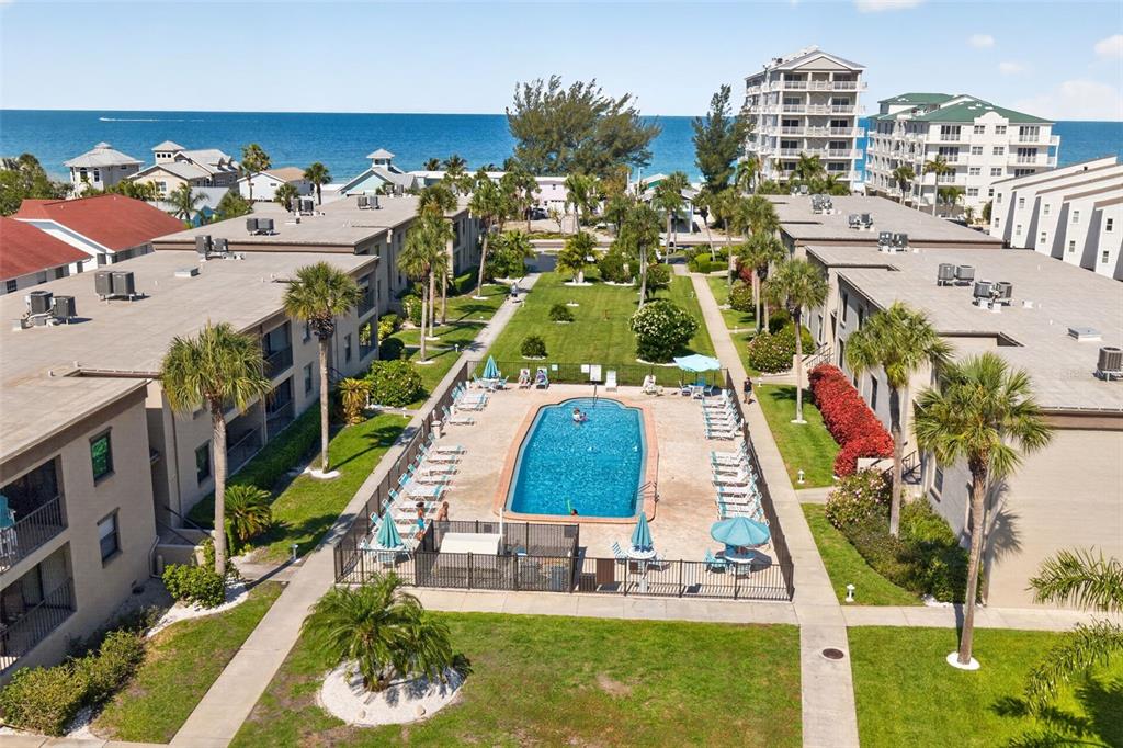 An aerial view shows a swimming pool situated between two apartment buildings near the ocean — 19725 GULF BOULEVARD UNIT 43, INDIAN SHORES, FL