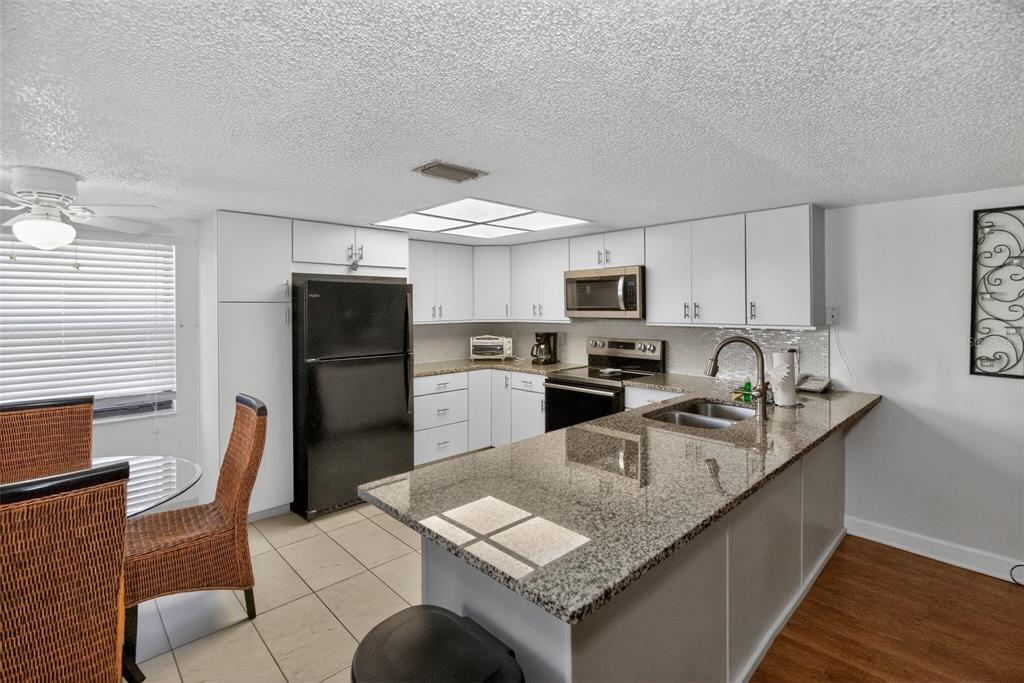 A kitchen features white cabinets, granite countertops, a black refrigerator, and a breakfast bar — 19725 GULF BOULEVARD UNIT 43, INDIAN SHORES, FL