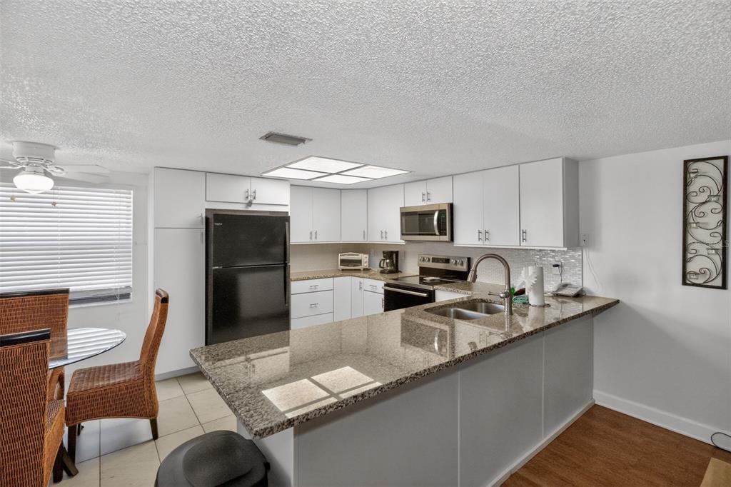 A kitchen features white cabinets, granite countertops, a black refrigerator, and a breakfast dining area — 19725 GULF BOULEVARD UNIT 43, INDIAN SHORES, FL