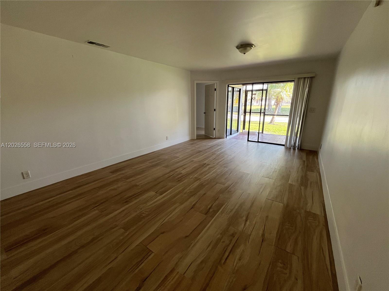 An empty room features light wood-look flooring, white walls, and a sliding glass door — 2501 NW 56th Ave # 14, Lauderhill FL 33313, LAUDERHILL, FL