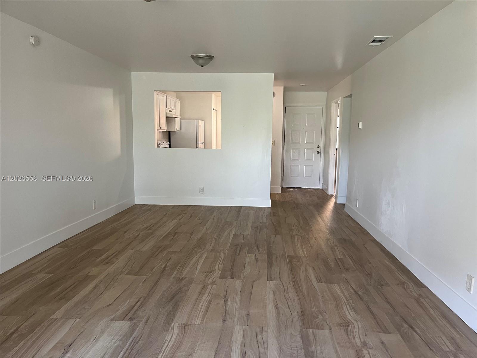 An empty room features light wood-look flooring, white walls, and a pass-through window to the kitchen — 2501 NW 56th Ave # 14, Lauderhill FL 33313, LAUDERHILL, FL