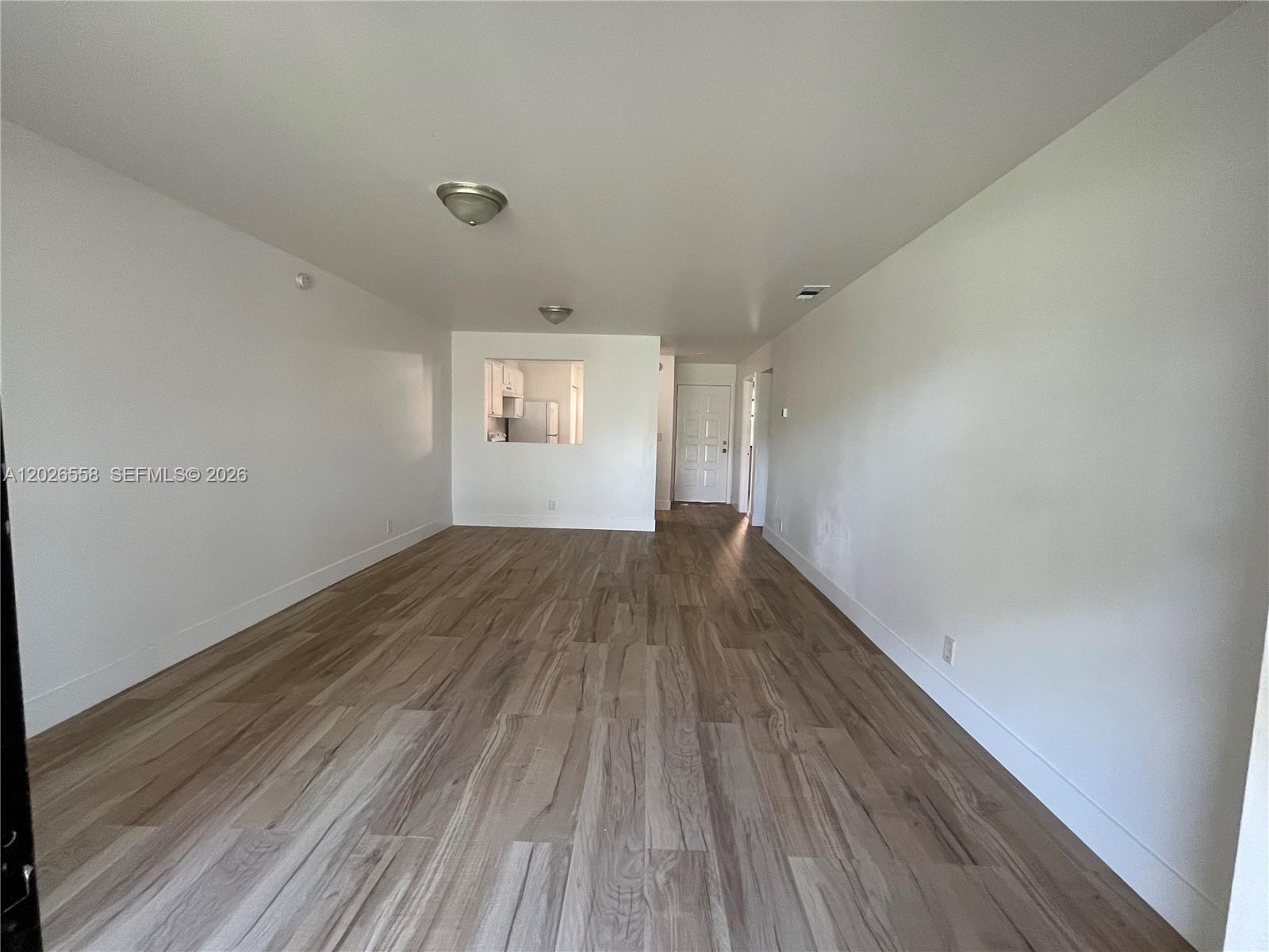 An empty living area features light wood-look flooring, white walls, and a kitchen pass-through window — 2501 NW 56th Ave # 14, Lauderhill FL 33313, LAUDERHILL, FL
