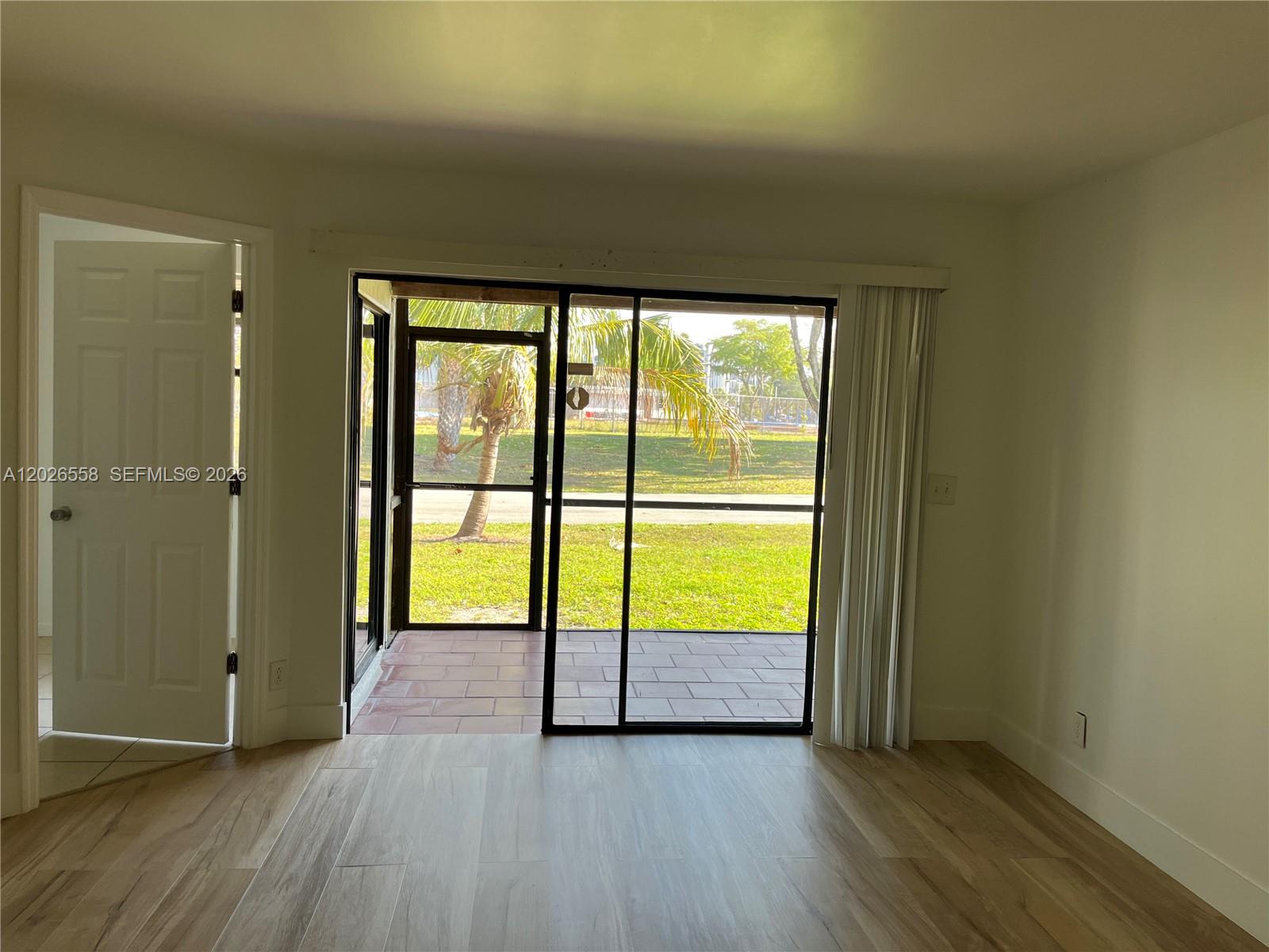 A room with light wood-look flooring leads to a screened patio through sliding glass doors — 2501 NW 56th Ave # 14, Lauderhill FL 33313, LAUDERHILL, FL