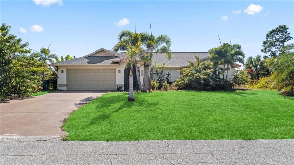 A single-story house with a beige exterior, a two-car garage, and a palm-filled front yard — 11195 SEABREEZE AVENUE, PORT CHARLOTTE, FL