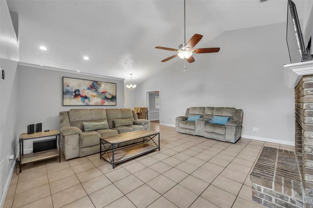A living room features a vaulted ceiling, tile flooring, two gray sofas, and a fireplace — 1921 BLUE FOX COURT, ORLANDO, FL