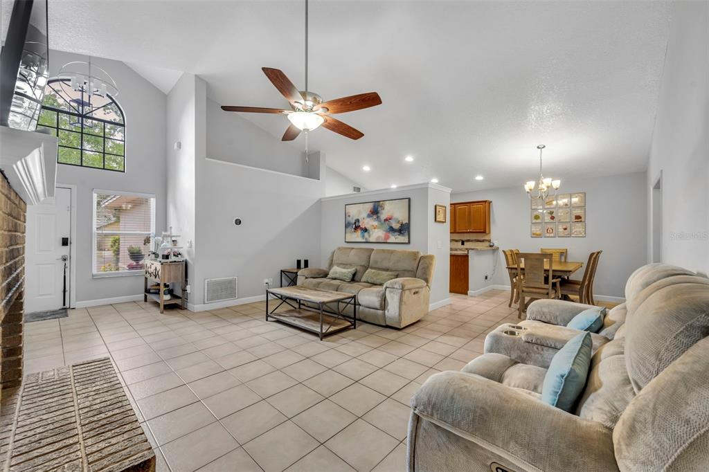 A living room with tile floors, a vaulted ceiling, a ceiling fan, and dining area — 1921 BLUE FOX COURT, ORLANDO, FL