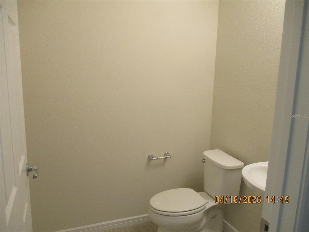 A small half bathroom features a white toilet, a pedestal sink, and beige walls — 1608 ASPEN AVE, DAVENPORT, FL