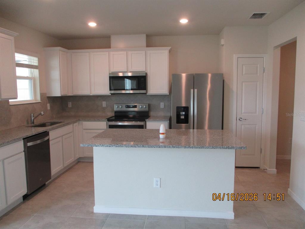A kitchen features white cabinets, granite countertops, stainless steel appliances, and a central island — 1608 ASPEN AVE, DAVENPORT, FL