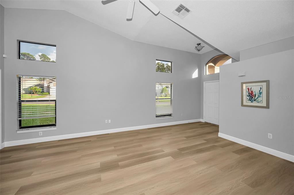 An empty living room features vaulted ceilings, light wood-look flooring, and multiple windows — 6240 FAIRSKIES DRIVE, NEW PORT RICHEY, FL
