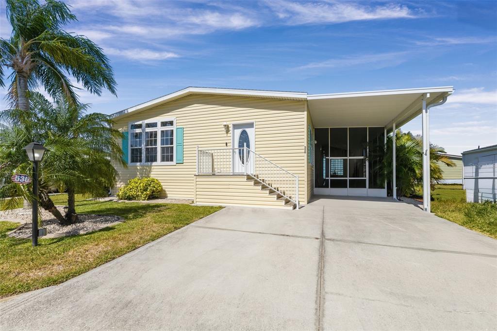 A yellow manufactured home features a concrete driveway, a carport, and a small front staircase — 530 SAN CLEMENTE CIRCLE, NORTH PORT, FL