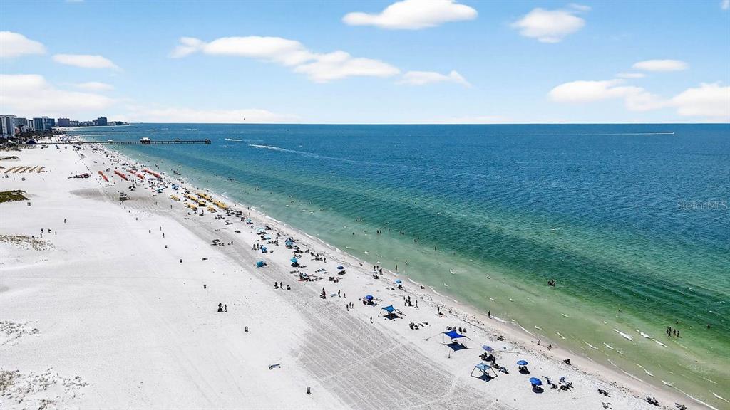 An aerial view shows a sandy beach with umbrellas and a pier extending into the ocean — 26 CAMBRIA STREET, CLEARWATER BEACH, FL
