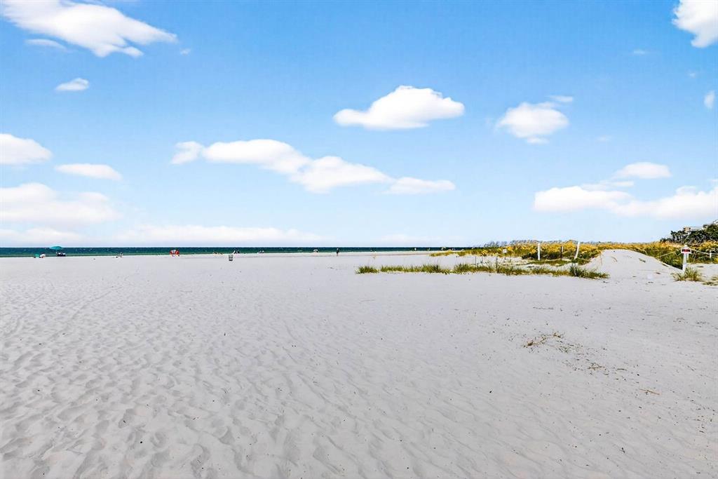 A wide, sandy beach stretches toward the ocean under a bright, partly cloudy blue sky — 26 CAMBRIA STREET, CLEARWATER BEACH, FL