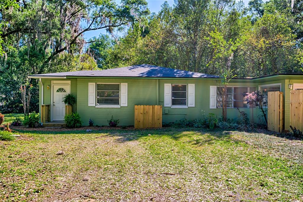 A single-story green house with a white front door and wooden privacy screens — 725 NW 33RD AVENUE, GAINESVILLE, FL