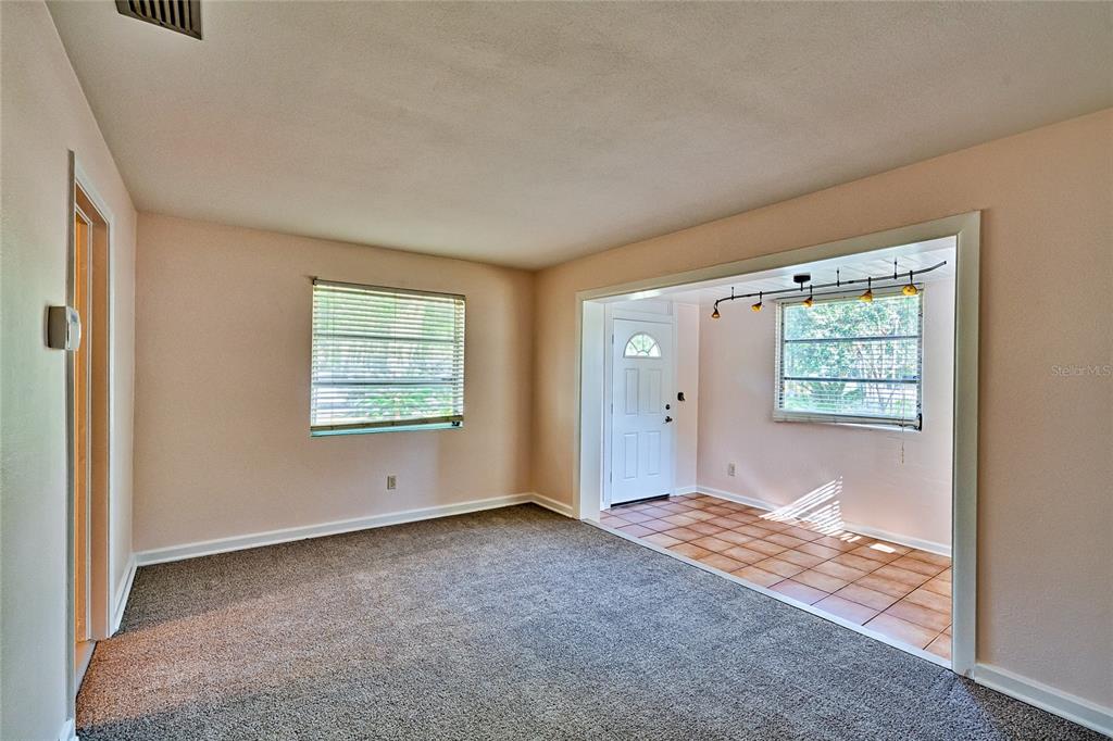A carpeted living room opens into a tiled entryway with a front door and windows — 725 NW 33RD AVENUE, GAINESVILLE, FL