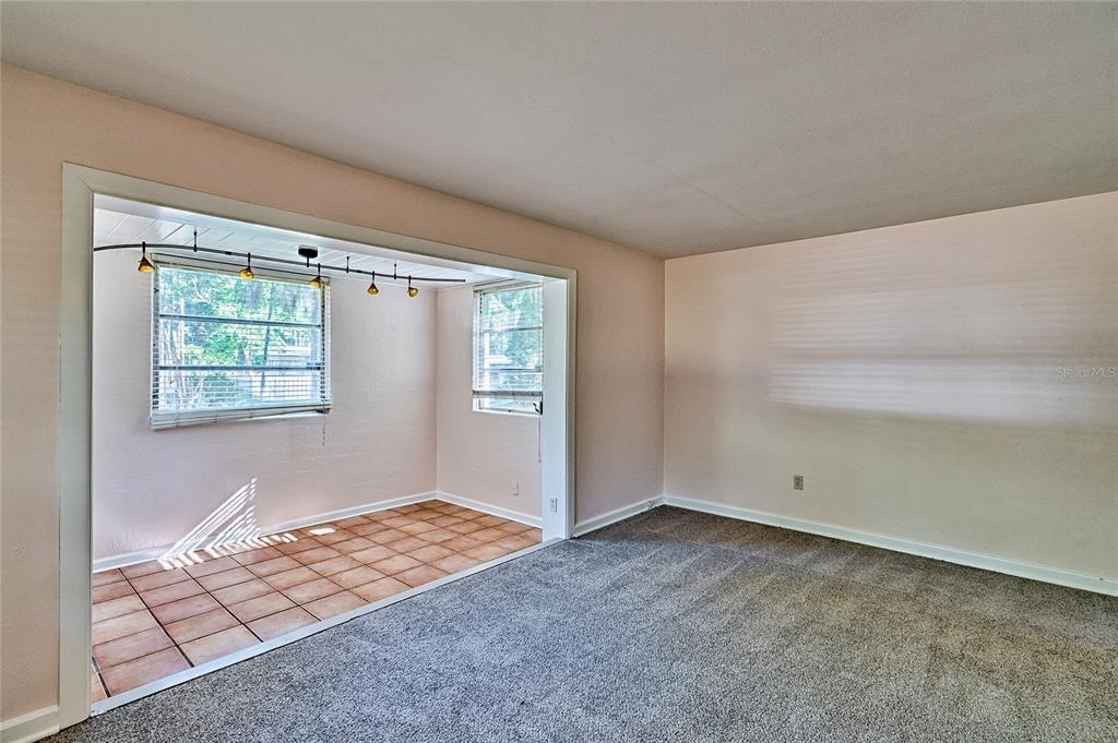 A carpeted living room opens into a tiled sunroom with large windows and track lighting — 725 NW 33RD AVENUE, GAINESVILLE, FL