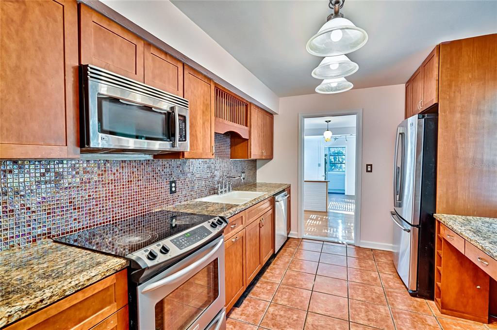 A kitchen with wood cabinets, granite countertops, stainless steel appliances, and a mosaic tile backsplash — 725 NW 33RD AVENUE, GAINESVILLE, FL