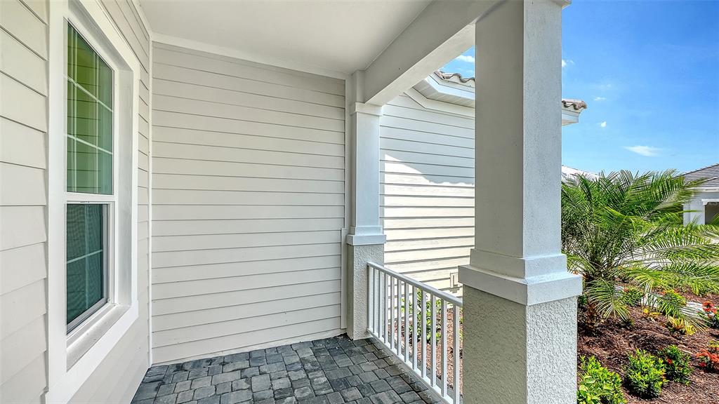 A covered porch features light-colored siding, a stone paver floor, and a white railing — 6336 LAKE WOODRUFF COURT, SARASOTA, FL