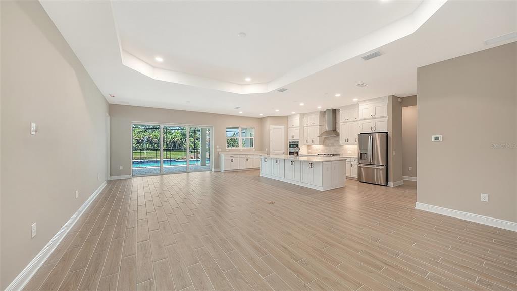 An open-concept kitchen and living area with light wood-look tile floors and a pool view — 6336 LAKE WOODRUFF COURT, SARASOTA, FL