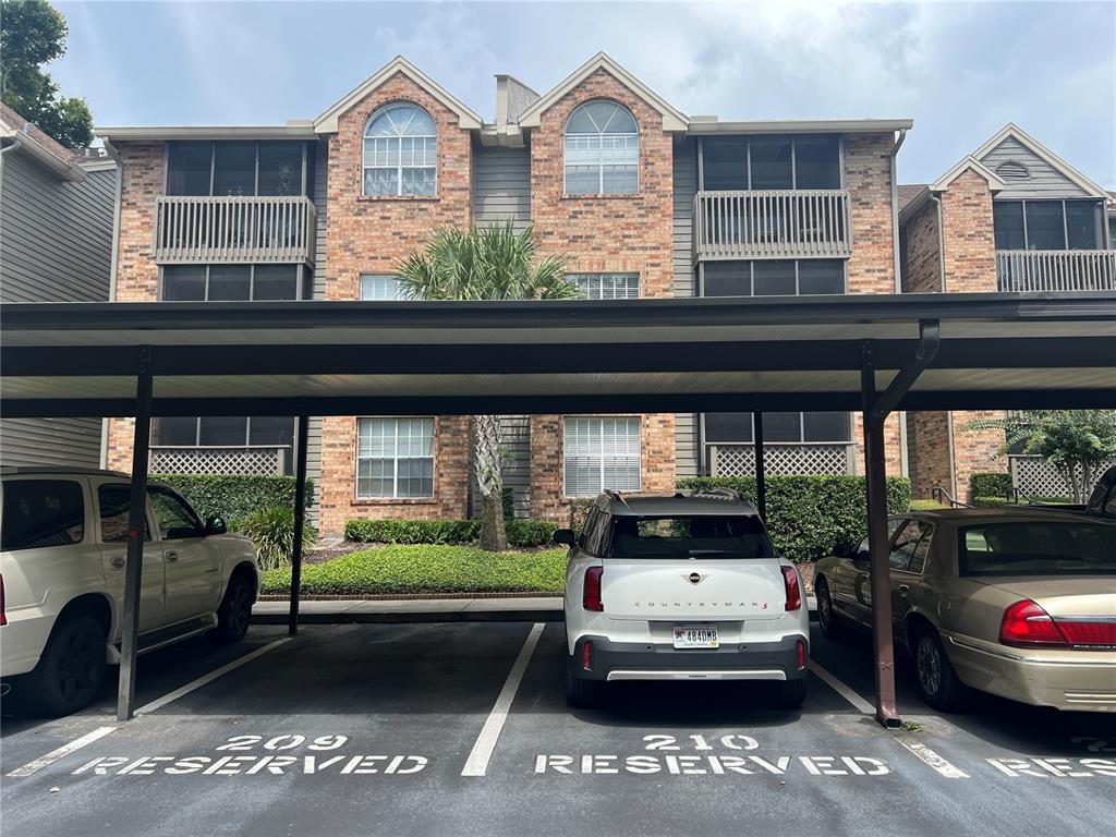 A three-story brick apartment building features covered parking spaces labeled 209 and 210 — 2500 WINDING CREEK BOULEVARD UNIT E103, CLEARWATER, FL