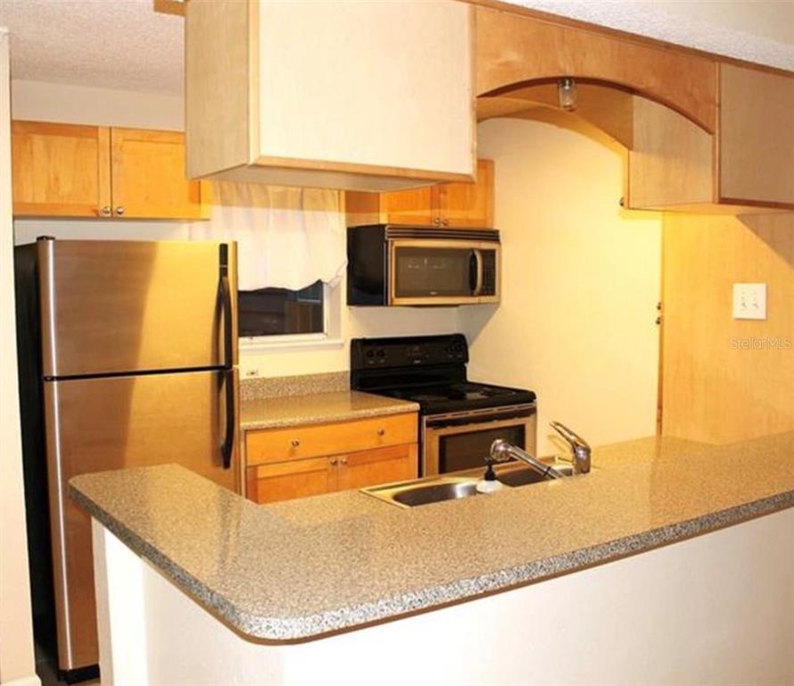 A kitchen features light wood cabinets, stainless steel appliances, and a granite-topped breakfast bar — 2500 WINDING CREEK BOULEVARD UNIT E103, CLEARWATER, FL