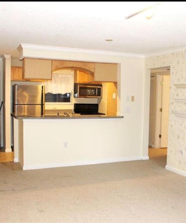 A kitchen with stainless steel appliances and wooden cabinets overlooks a carpeted living area — 2500 WINDING CREEK BOULEVARD UNIT E103, CLEARWATER, FL