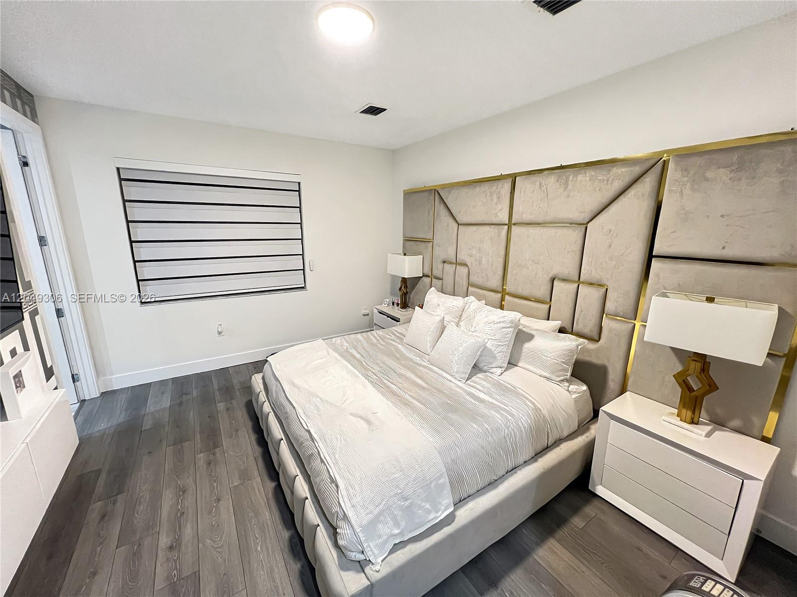 A bedroom features a large upholstered headboard with gold trim, white nightstands, and gray flooring — 4386 NW 80th Ct, Doral FL 33166, DORAL, FL