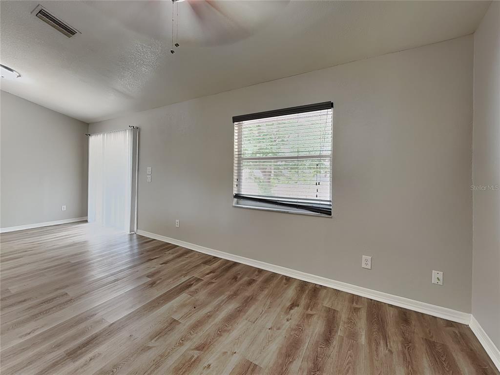 An empty room features light gray walls, wood-look flooring, a window with blinds, and sliding doors — 7352 BOLTEN LANE, PORT CHARLOTTE, FL