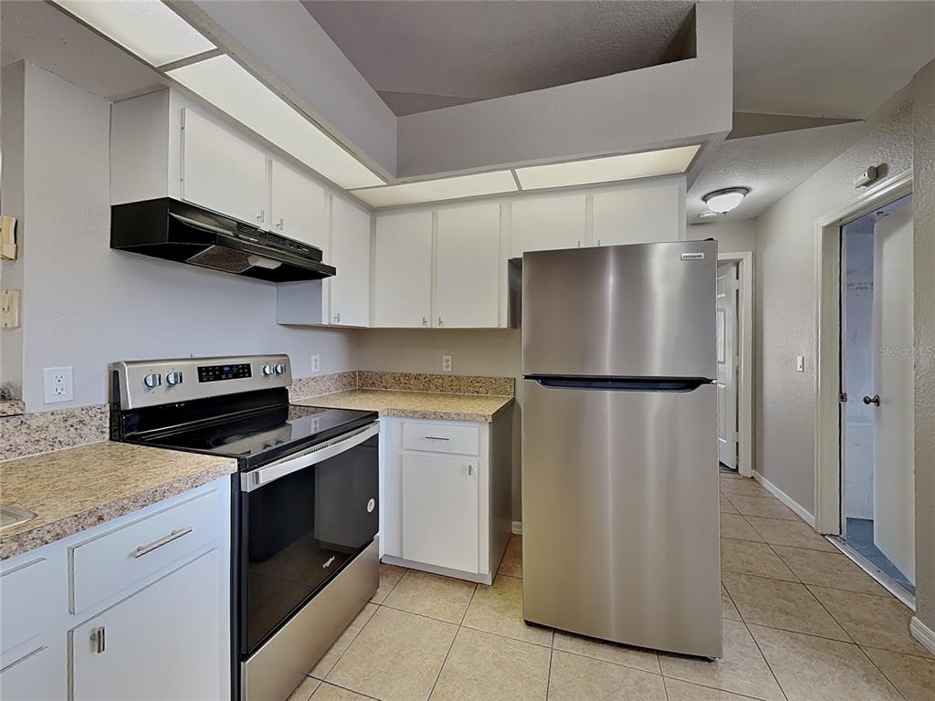 A kitchen features white cabinets, granite countertops, stainless steel appliances, and beige tile flooring — 7352 BOLTEN LANE, PORT CHARLOTTE, FL