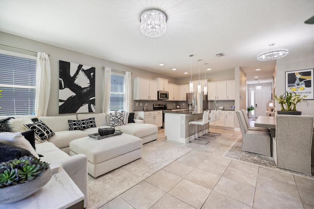 An open-concept living room and kitchen featuring white cabinetry, tile flooring, and a sectional sofa — 8660 ICE WINE STREET, SARASOTA, FL