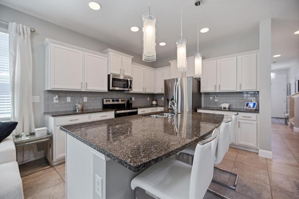 A kitchen with white cabinets, granite countertops, a central island, and three pendant lights — 8660 ICE WINE STREET, SARASOTA, FL