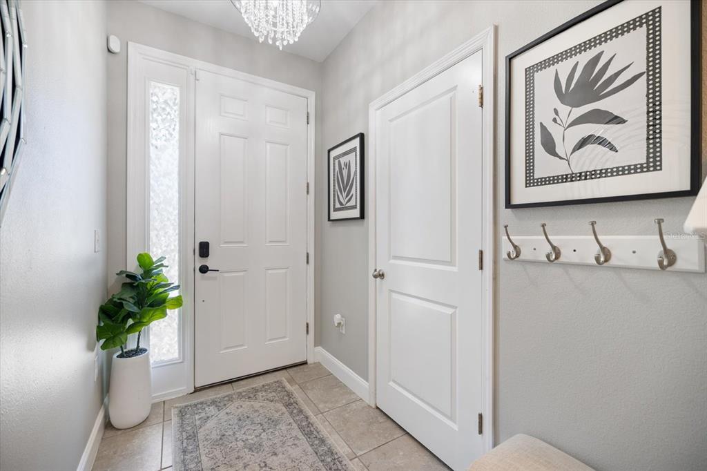 An entryway features a white front door, a coat rack, framed wall art, and tile flooring — 8660 ICE WINE STREET, SARASOTA, FL