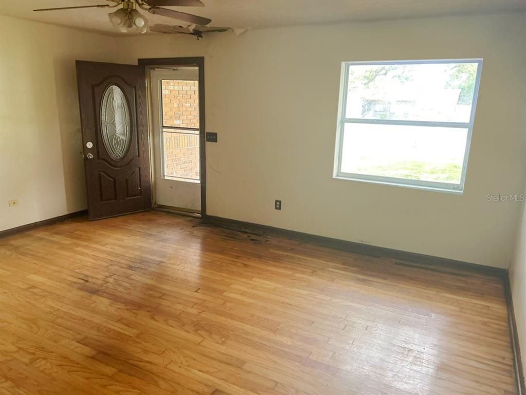 An empty room features hardwood floors, a ceiling fan, a window, and an open door — 1749 HAVERHILL DRIVE, DELTONA, FL