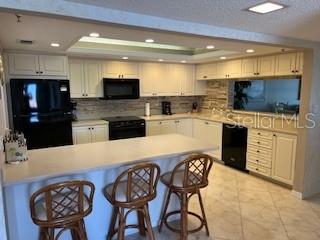 A kitchen features white cabinetry, black appliances, a breakfast bar with stools, and tile flooring — 1425 GULF OF MEXICO DRIVE UNIT 308, LONGBOAT KEY, FL