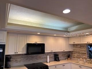 A kitchen features white cabinets, a black microwave, a stone backsplash, and a tray ceiling — 1425 GULF OF MEXICO DRIVE UNIT 308, LONGBOAT KEY, FL