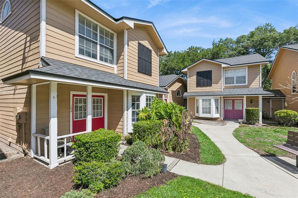 Two tan two-story townhouses with red and purple front doors sit along a concrete walkway — 5989 BRAEMAR PLACE UNIT 102, ORLANDO, FL