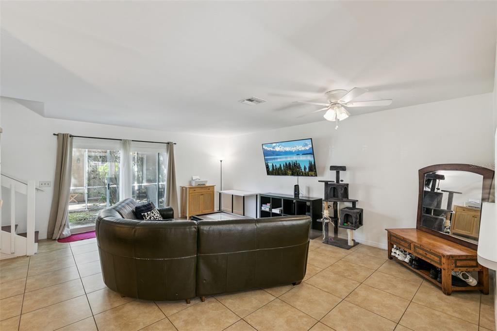 A living room features tile floors, a wooden coffee table, and a staircase with railings — 5989 BRAEMAR PLACE UNIT 102, ORLANDO, FL