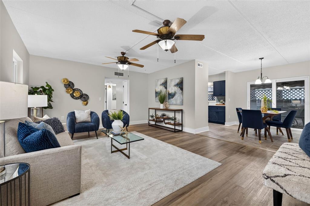 A living room with wood-look flooring, two ceiling fans, and an adjacent dining area — 1190 RUE DES CHATEAUX UNIT 1A, ST PETERSBURG, FL